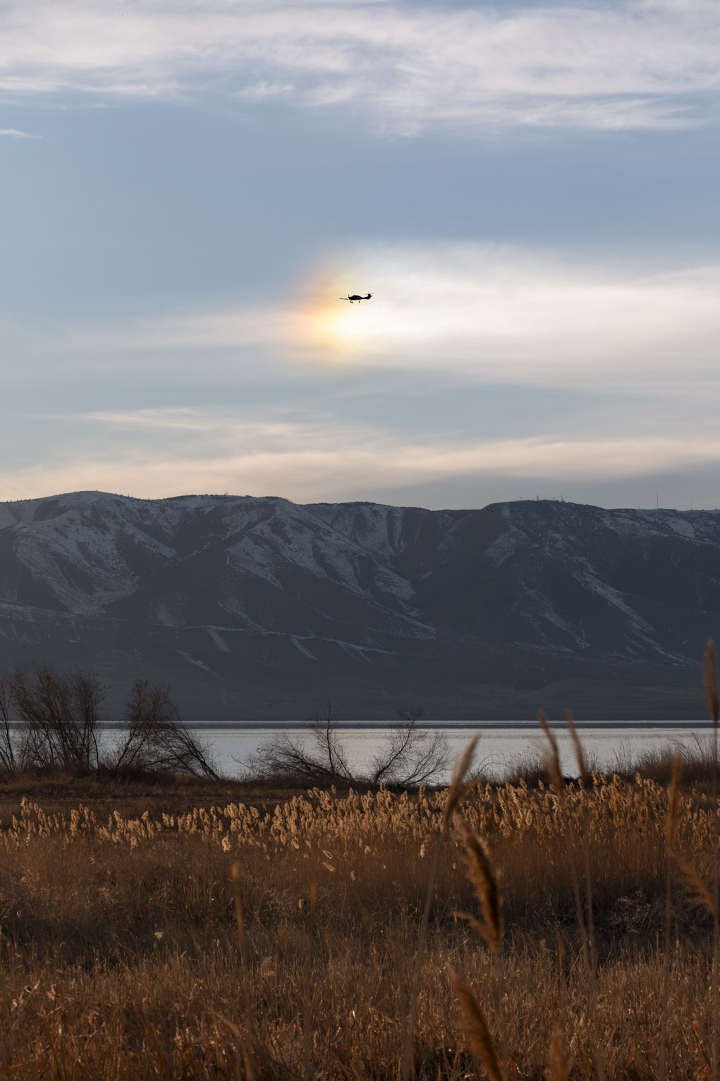 Over the lake and mountain a sun dog with a plane flying through it